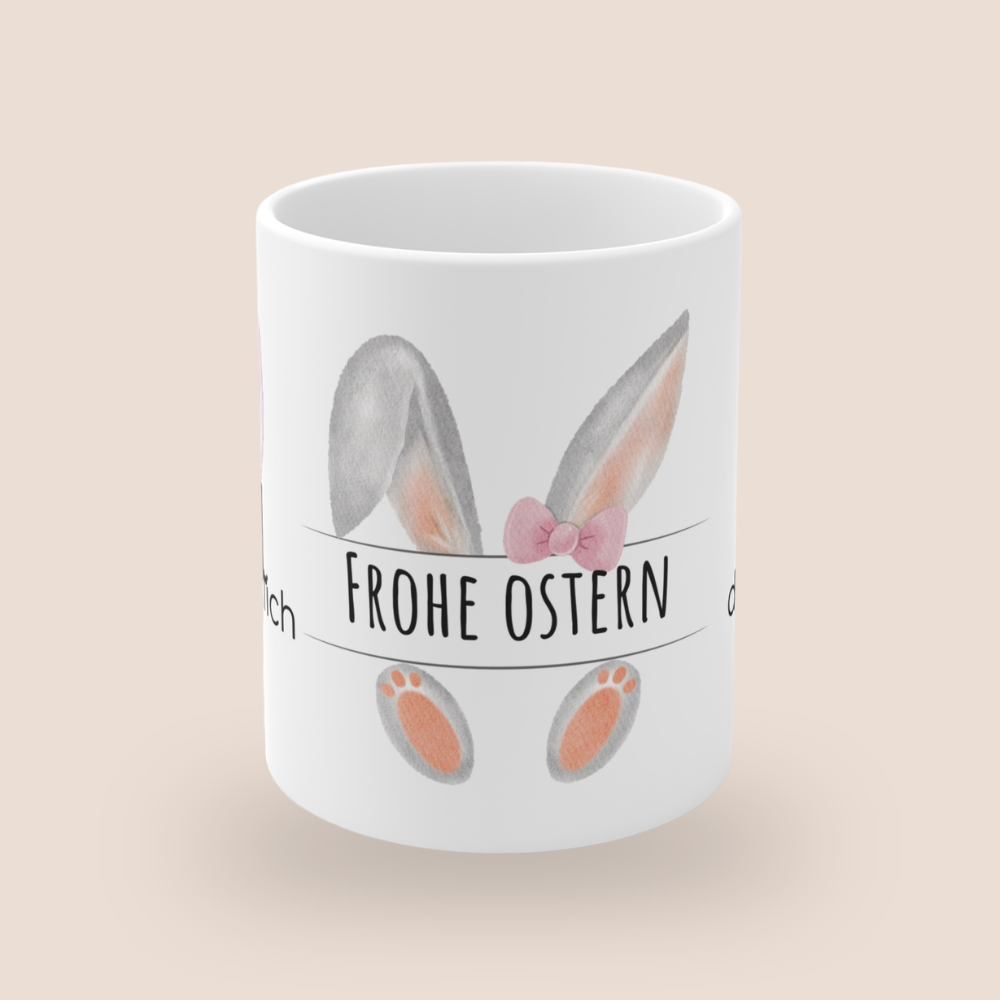 Weiße Keramiktasse mit dem Spruch „Hoppel dich glücklich“, rosa Hasenohren sowie dem Schriftzug „Frohe Ostern“ und einem niedlichen Osterhasen-Design – 300-ml-Tasse.
