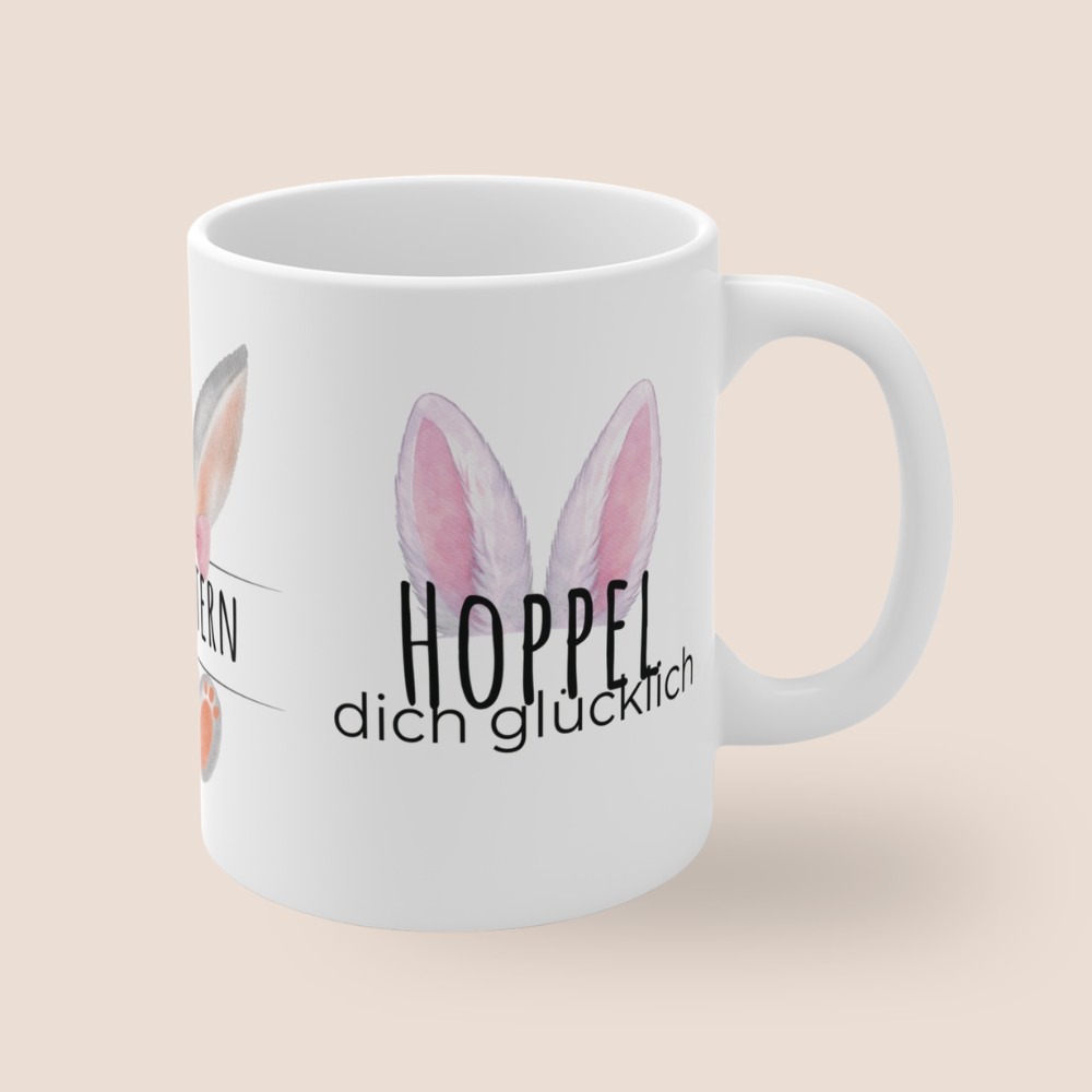 Weiße Keramiktasse mit dem Spruch „Hoppel dich glücklich“, rosa Hasenohren sowie dem Schriftzug „Frohe Ostern“ und einem niedlichen Osterhasen-Design – 300-ml-Tasse.