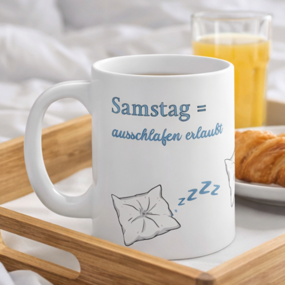 Weiße 300-ml-Keramiktasse mit schlafendem Kissen, blauen "Zzz" und dem Spruch „Samstag = Ausschlafen erlaubt“ – lustige Tasse für Langschläfer und entspannte Wochenenden.