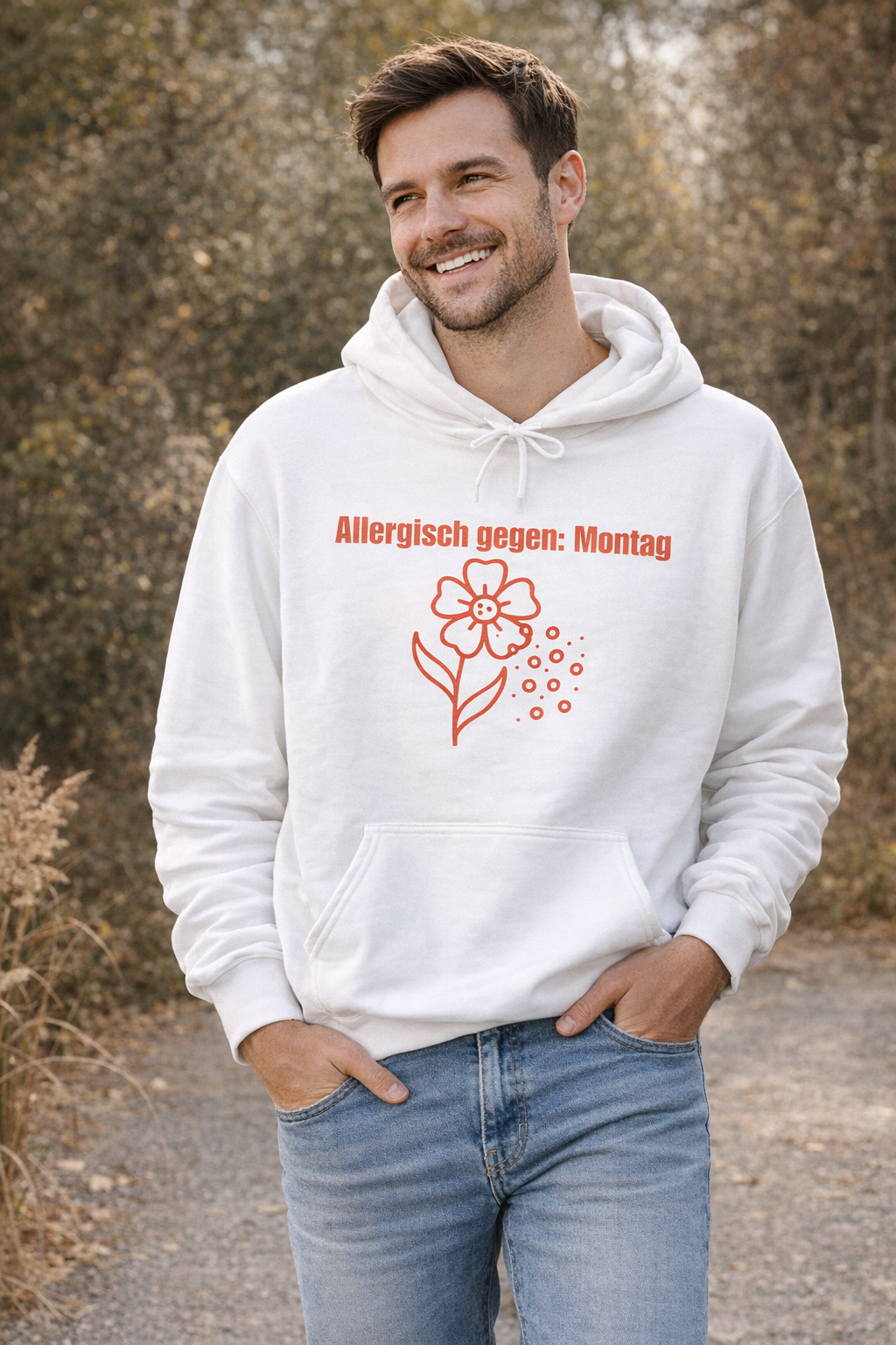 Weißer Unisex-Hoodie mit dem Spruch „Allergisch gegen Montag“ und humorvollem Blumenmotiv mit fliegenden Pollen auf der Vorderseite.