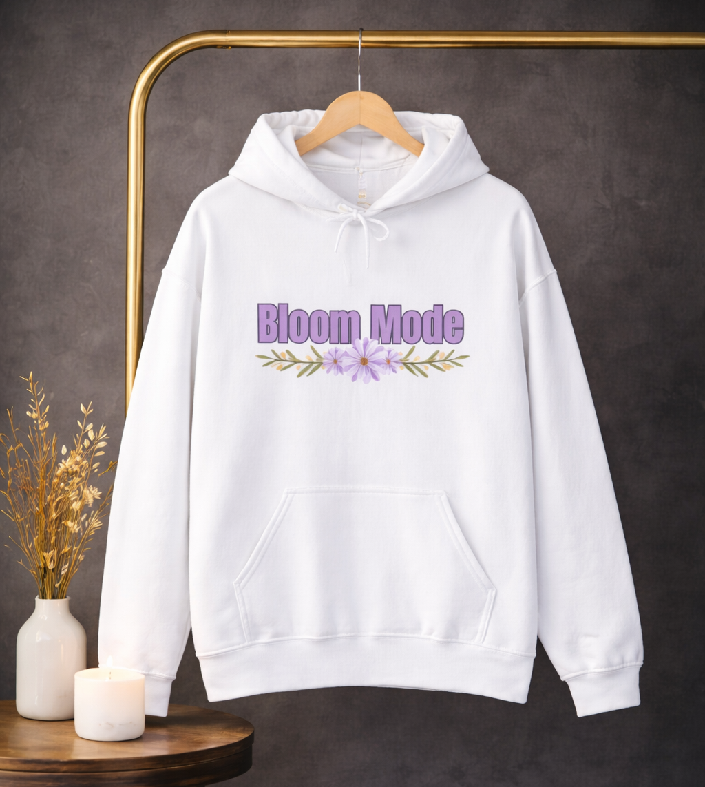 Weißer Unisex-Hoodie mit dem Schriftzug „Bloom Mode“ und einem floralen Blumenmotiv in Lilatönen auf der Vorderseite.
