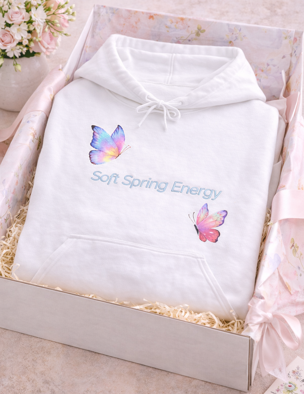 Weißer Unisex-Hoodie mit zwei bunten Schmetterlingen in Pastelltönen und dem Schriftzug „Soft Spring Energy“ auf der Vorderseite.
