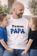 Weißes und hellblaues Unisex-Sweatshirt mit dem Schriftzug „Team Papa“ in Schwarz und Blau sowie dekorativen Schnurrbart-Elementen.