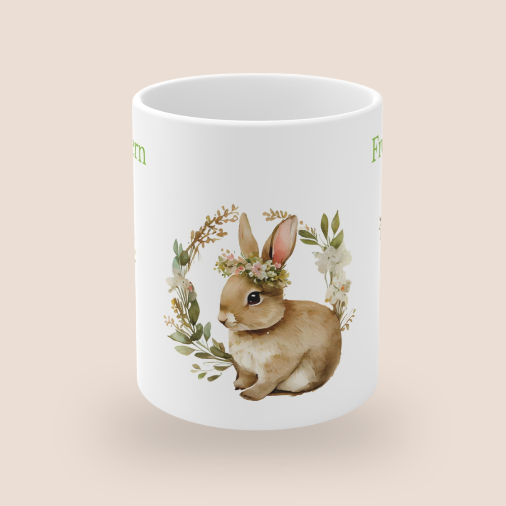 Weiße Keramiktasse mit dem Schriftzug „Frohe Ostern“, einem niedlichen Aquarell-Hasen mit Blumenkranz sowie dekorativen Osterzweigen mit bunten Ostereiern – 300-ml-Ostertasse.