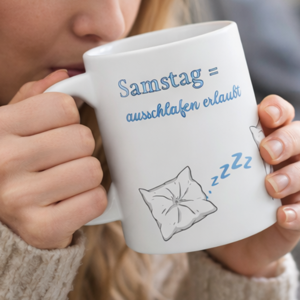 Weiße 300-ml-Keramiktasse mit schlafendem Kissen, blauen "Zzz" und dem Spruch „Samstag = Ausschlafen erlaubt“ – lustige Tasse für Langschläfer und entspannte Wochenenden.