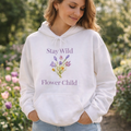 Weißer Unisex-Hoodie mit Wildblumen-Motiv und dem Schriftzug „Stay Wild Flower Child“ in sanften Lilatönen auf der Vorderseite.