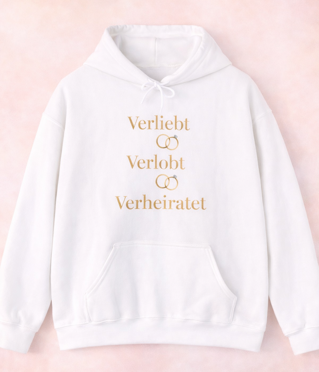 Weißer Unisex Hoodie mit dem eleganten Schriftzug „Verliebt Verlobt Verheiratet“ und dezenten Eheringen – romantischer Hoodie für Paare und Hochzeiten.