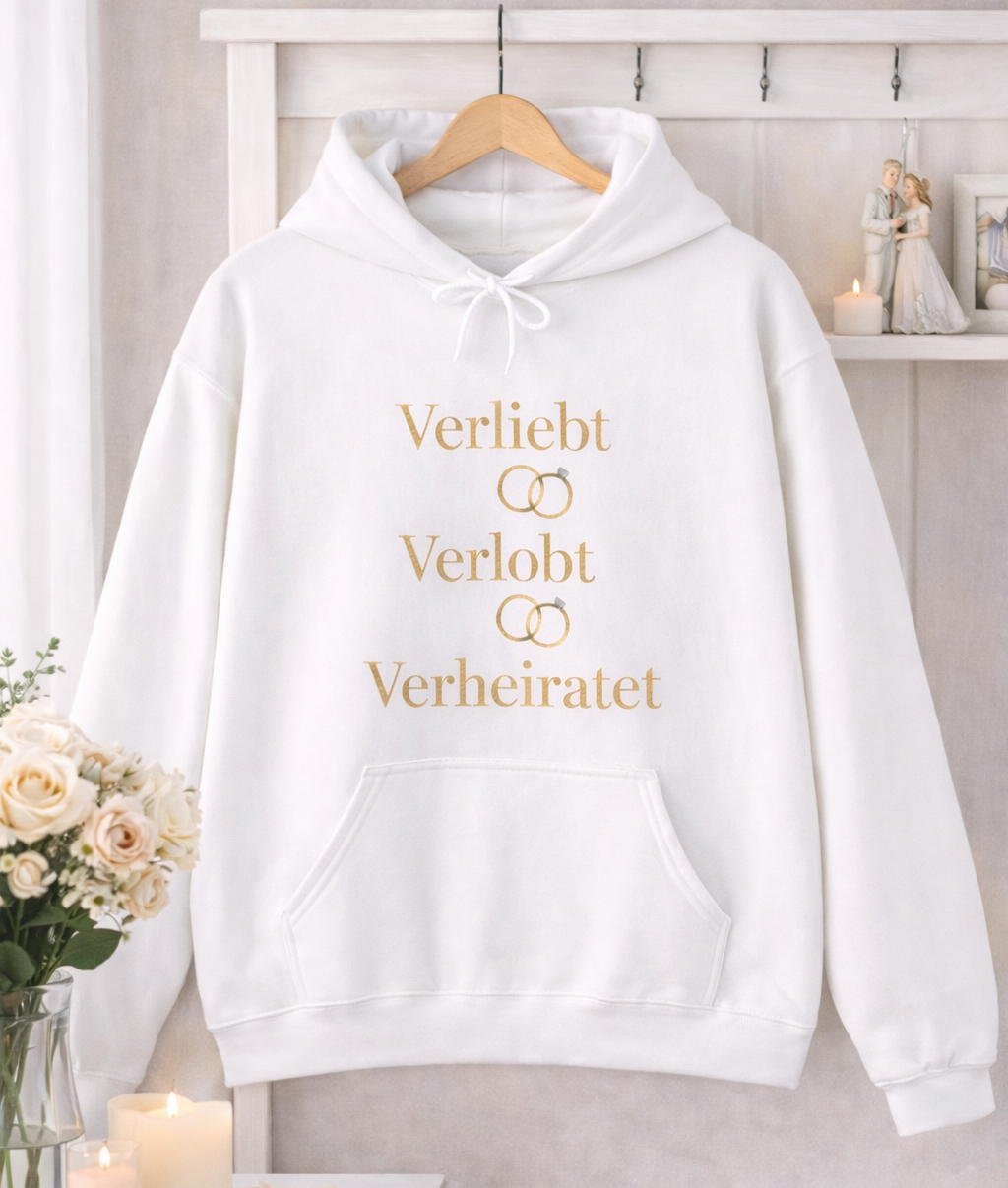 Weißer Unisex Hoodie mit dem eleganten Schriftzug „Verliebt Verlobt Verheiratet“ und dezenten Eheringen – romantischer Hoodie für Paare und Hochzeiten.