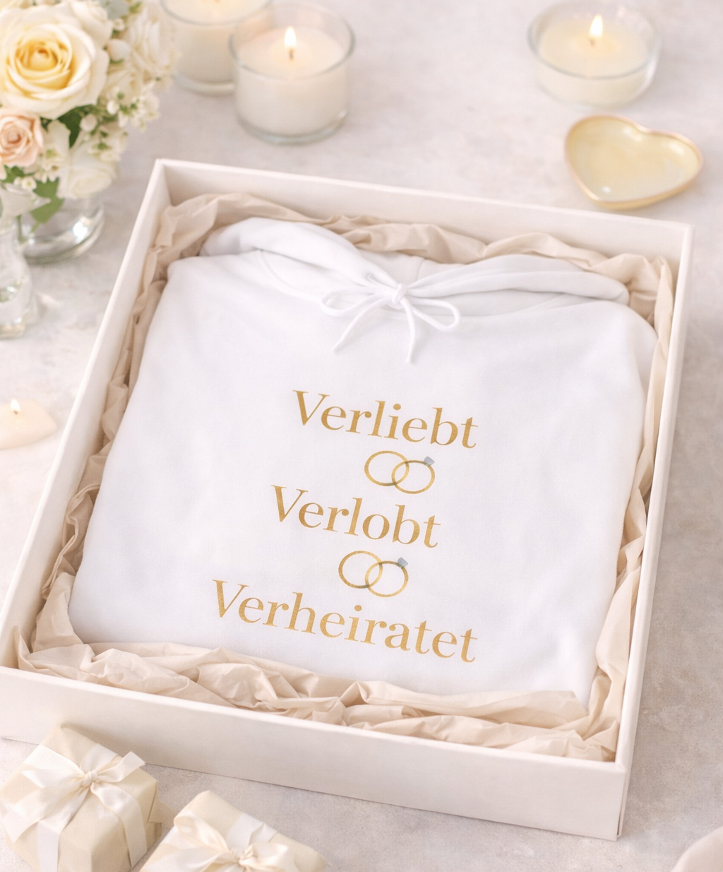 Weißer Unisex Hoodie mit dem eleganten Schriftzug „Verliebt Verlobt Verheiratet“ und dezenten Eheringen – romantischer Hoodie für Paare und Hochzeiten.