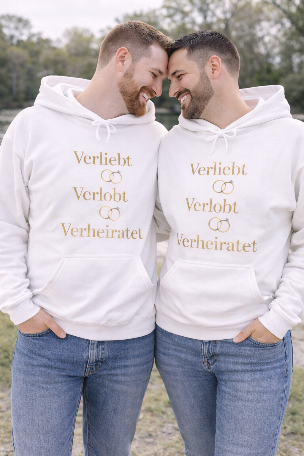 Weißer Unisex Hoodie mit dem eleganten Schriftzug „Verliebt Verlobt Verheiratet“ und dezenten Eheringen – romantischer Hoodie für Paare und Hochzeiten.