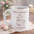 Weiße Keramiktasse mit dem Spruch „Kaffee schmeckt im Frühling besser“, einer minimalistischen Kaffeetasse, Kaffeebohnen und Herzmotiven in warmen Braun- und Rosatönen.