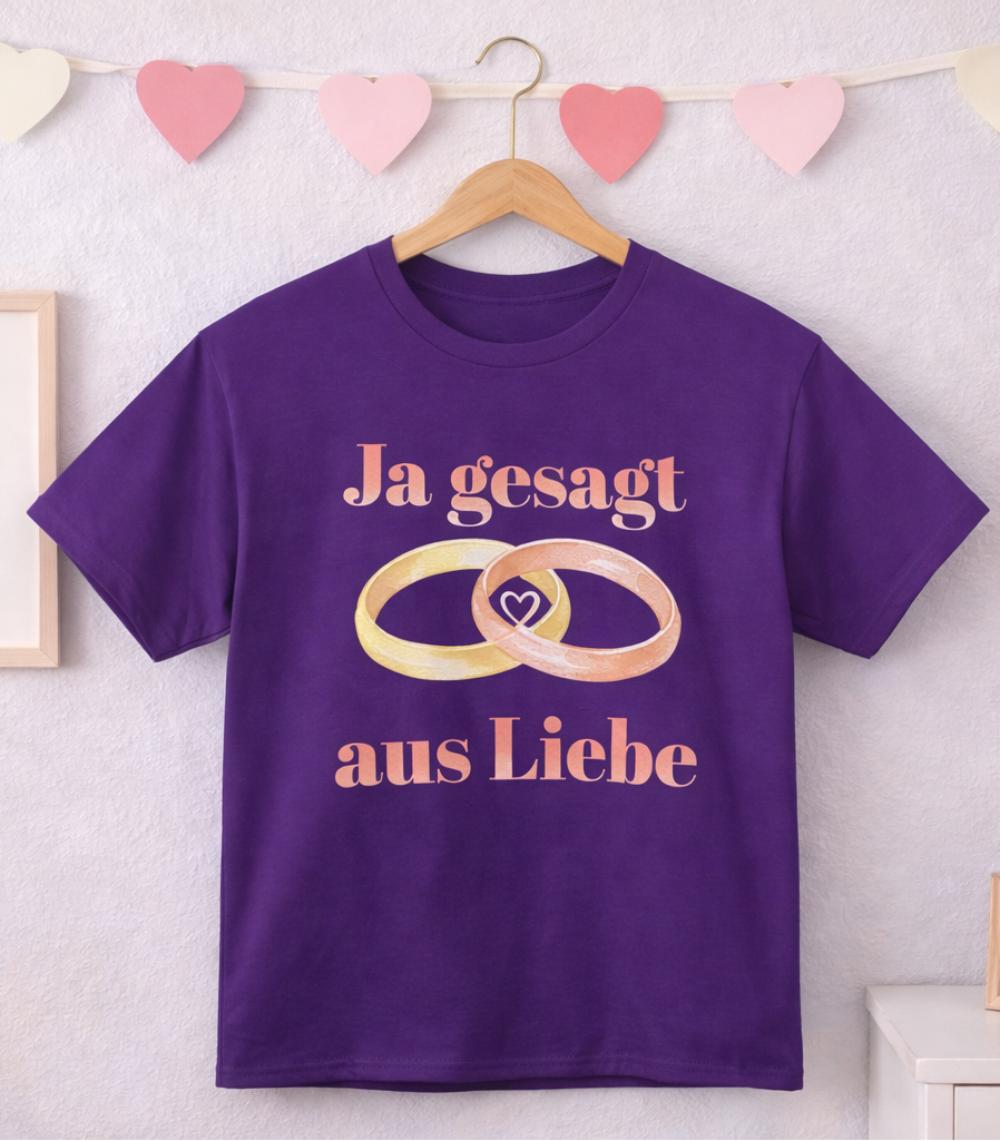 Unisex T-Shirt mit dem Schriftzug „Ja gesagt aus Liebe“ und zwei ineinander verschlungenen Eheringen in Gold und Roségold als romantisches Hochzeitsmotiv.