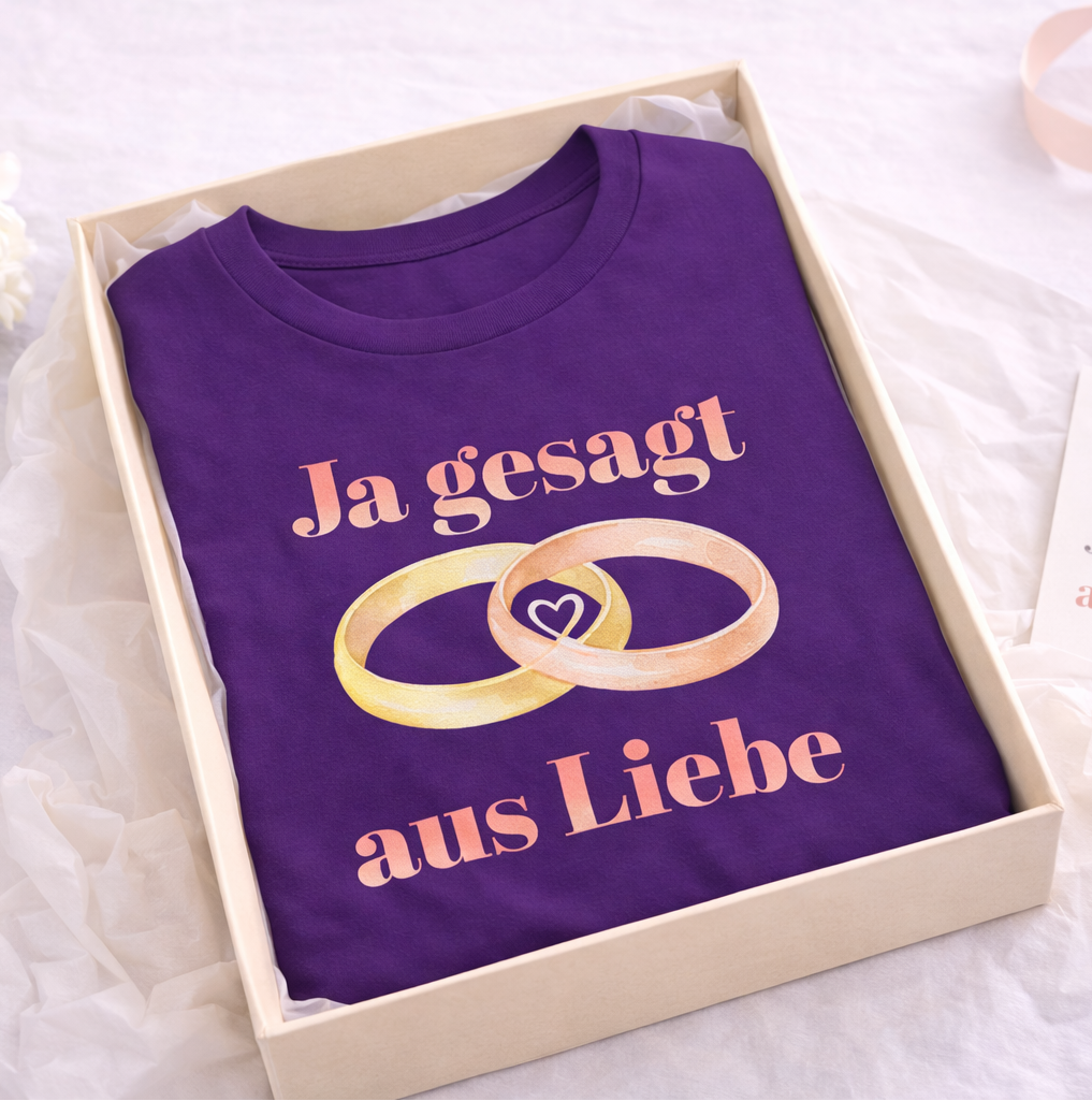 Unisex T-Shirt mit dem Schriftzug „Ja gesagt aus Liebe“ und zwei ineinander verschlungenen Eheringen in Gold und Roségold als romantisches Hochzeitsmotiv.
