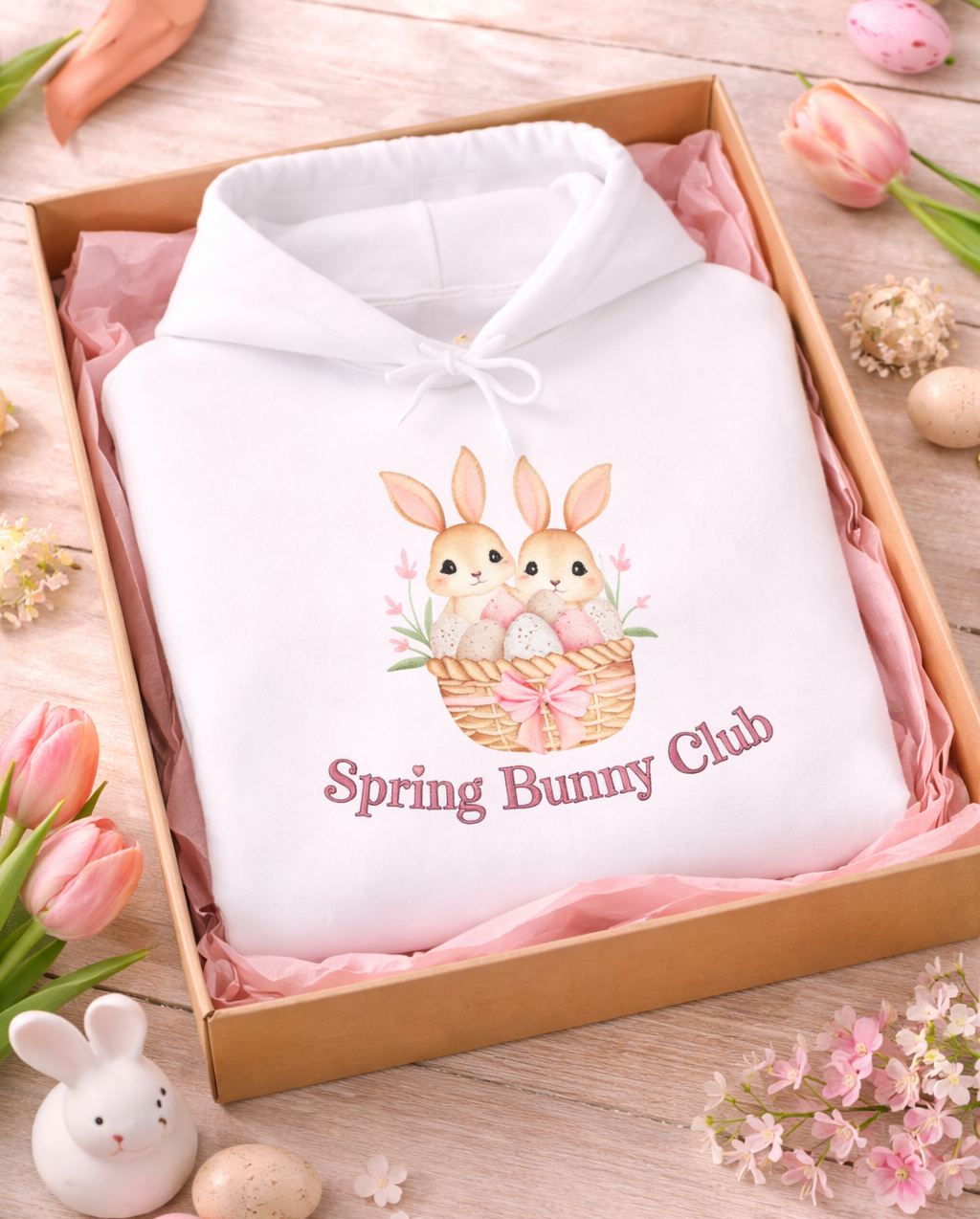 Weißer Unisex-Hoodie mit zwei süßen Hasen in einem Osterkörbchen und dem Schriftzug „Spring Bunny Club“ auf der Vorderseite.