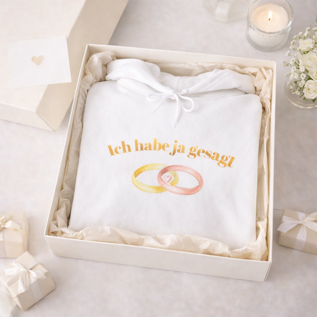 Weißer Unisex Hoodie mit dem Schriftzug „Ich habe Ja gesagt“ und zwei ineinander verschlungenen Eheringen als romantisches Hochzeitsmotiv.
