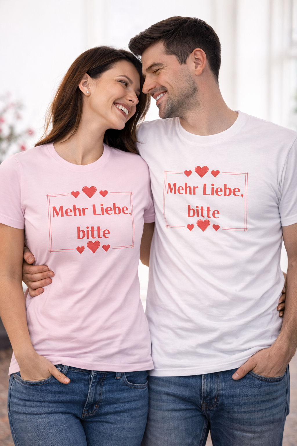 Unisex T-Shirt mit dem Schriftzug „Mehr Liebe, bitte“, dekorativen Herzen und schlichtem romantischem Design in Rot auf weißem oder rosafarbenem Shirt.