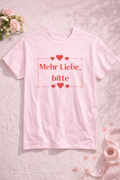 Unisex T-Shirt mit dem Schriftzug „Mehr Liebe, bitte“, dekorativen Herzen und schlichtem romantischem Design in Rot auf weißem oder rosafarbenem Shirt.