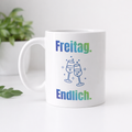 Weiße 300-ml-Keramiktasse mit dem Spruch „Freitag. Endlich.“ und zwei anstoßenden Gläsern – moderne Bürotasse für Feierabend und Wochenende.